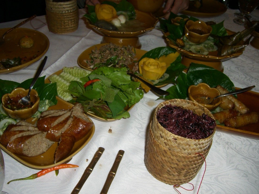 Table de plats laotiens : saucisse, salade d’herbes, riz gluant en panier tressé